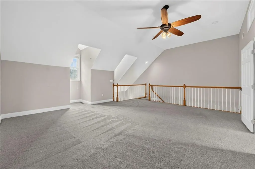 Spacious loft area featuring sloped ceilings, light gray carpeting, and a ceiling fan with integrated lighting