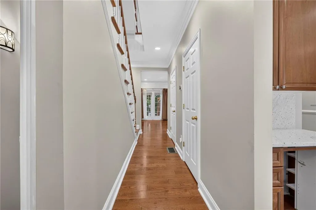 Hardwood flooring throughout the hallway, featuring a white staircase with wood railings, recessed lighting, and crown molding