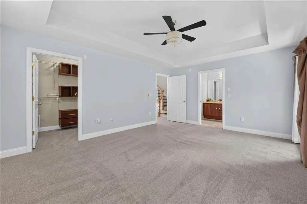 Spacious carpeted room featuring a tray ceiling with a ceiling fan, light blue walls, and white trim