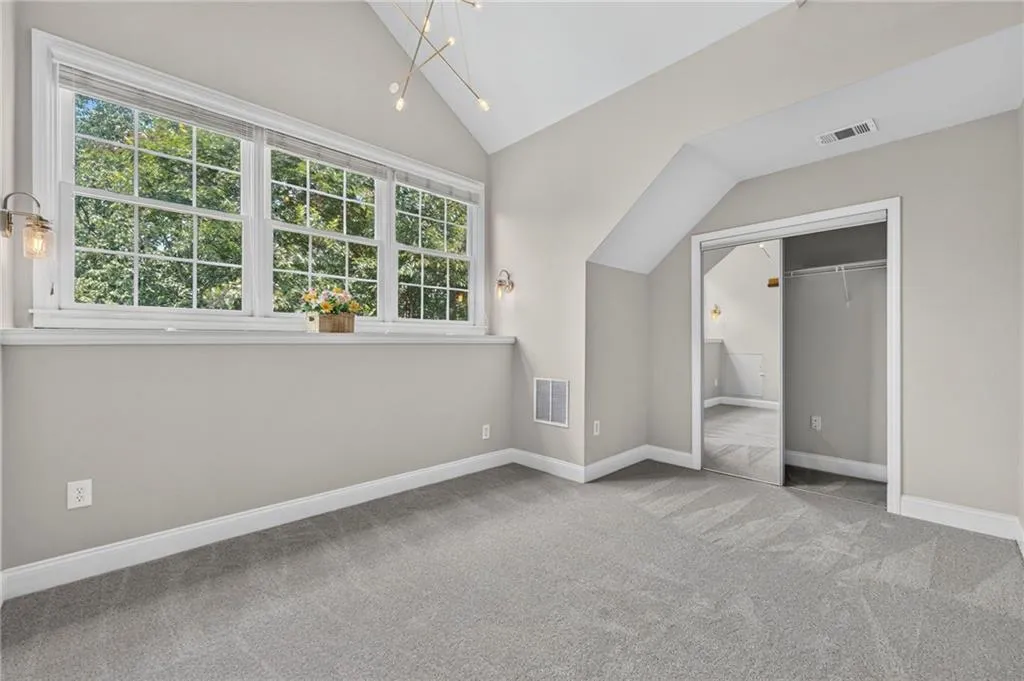 Room featuring vaulted ceilings, plush grey carpeting, and a large window with white muntins