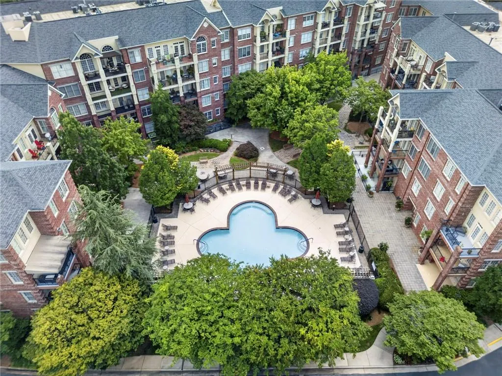 Central courtyard featuring a clover-shaped swimming pool with an expansive sundeck, surrounded by mature landscaping and multi-story brick buildings with private balconies
