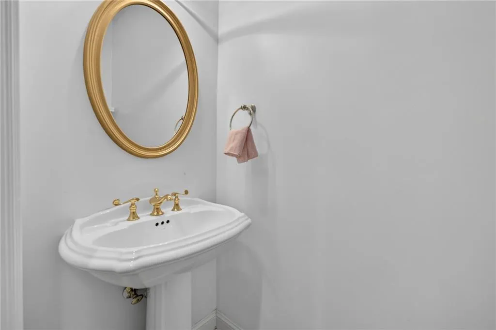 White pedestal sink with a decorative basin, brass-finish faucet, and an oval mirror with a brass-finish frame