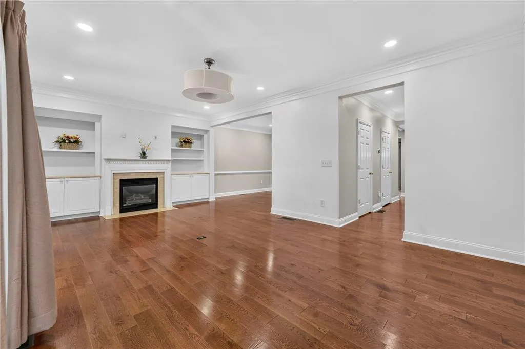 Spacious living area featuring wood-finish flooring, a fireplace with a stone surround, built-in shelving and cabinetry, recessed lighting, and crown molding