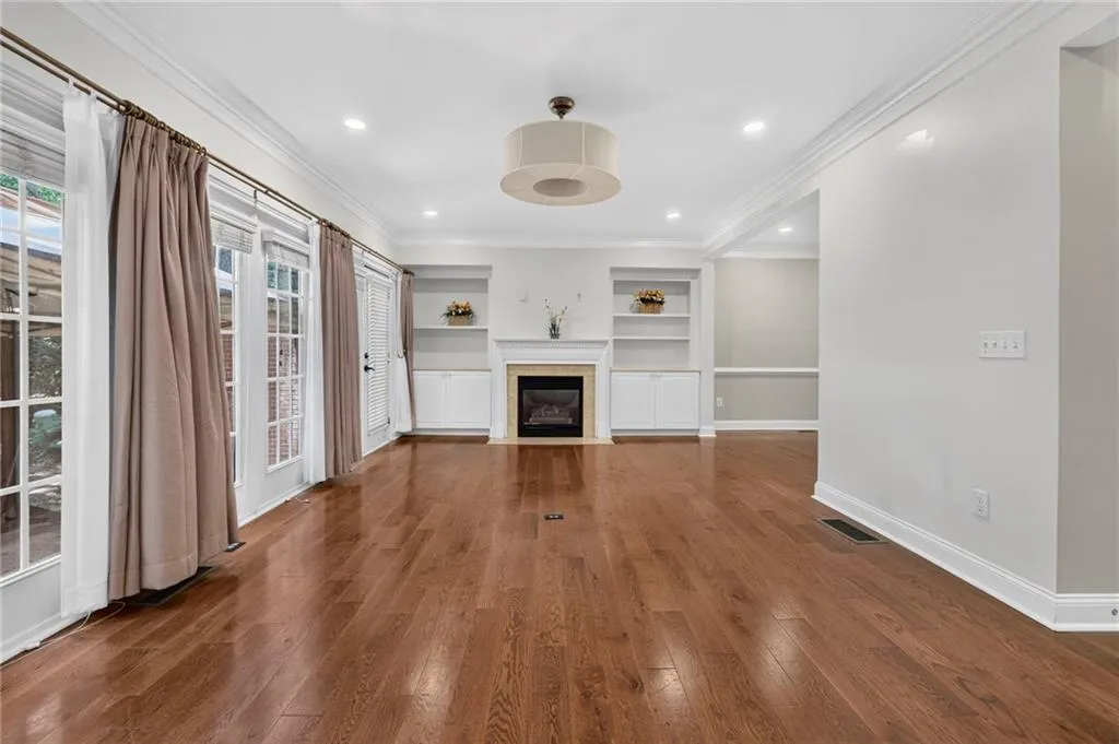 Spacious room featuring wood-finish flooring, a central fireplace with built-in cabinetry and shelving, multiple French doors, recessed lighting, and crown molding