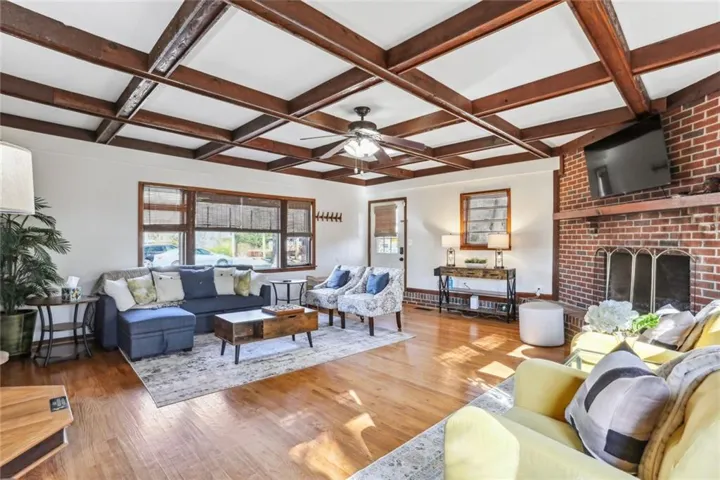 Living room featuring ceiling fan, dark wood-type flooring, beam ceiling, coffered ceiling, and a fireplace