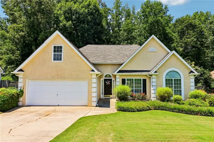 Stucco exterior with gabled roofline, arched front window, decorative shutters, and an attached two-car garage