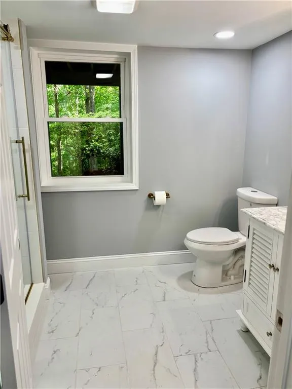 Full bath with marble finish floors, baseboards, toilet, and a stall shower