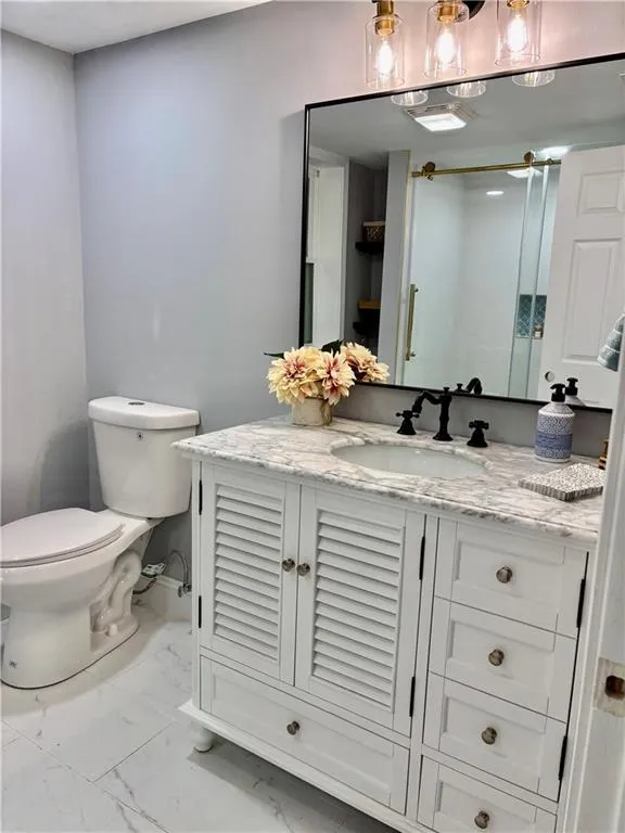 Bathroom with marble look tiles, toilet, vanity, and baseboards