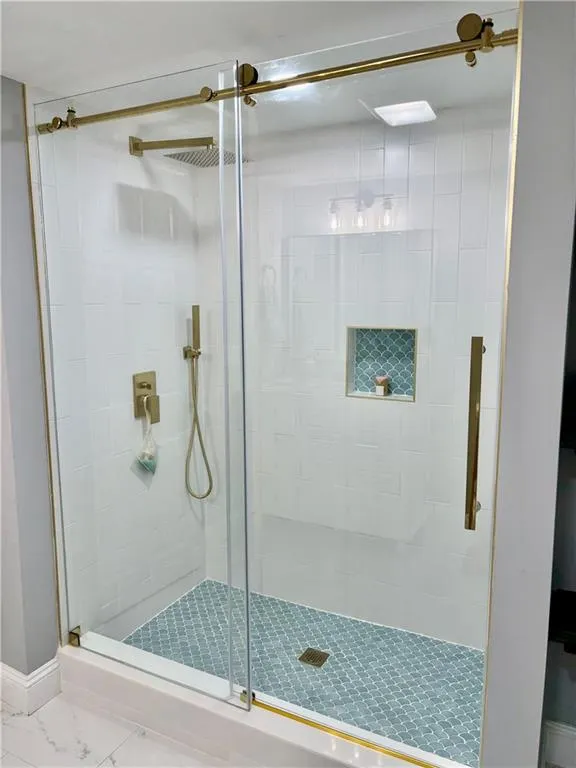 Full bathroom featuring a shower stall, marble look tile flooring, and baseboards
