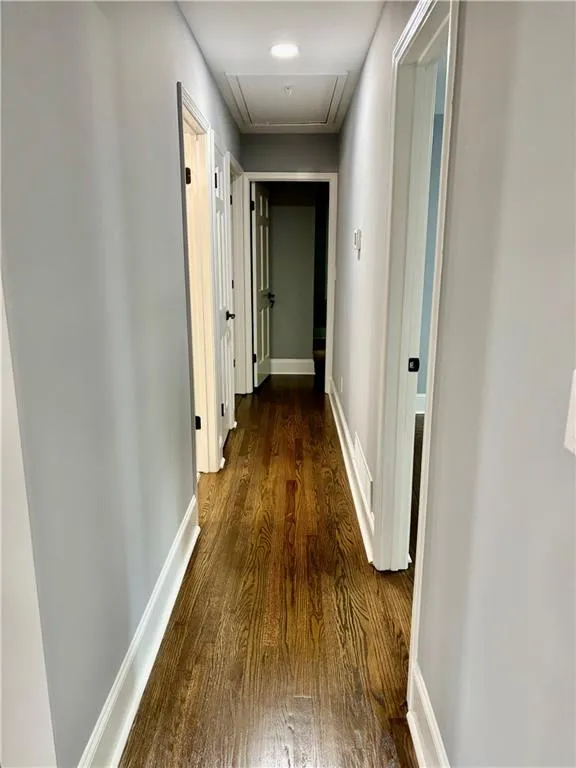 Corridor with attic access, dark wood-style floors, and baseboards