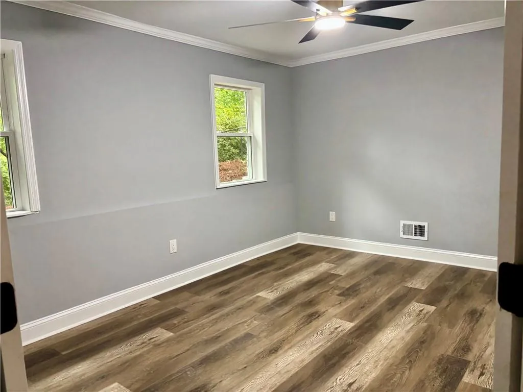 Spare room featuring a ceiling fan, baseboards, crown molding, and dark wood-style floors