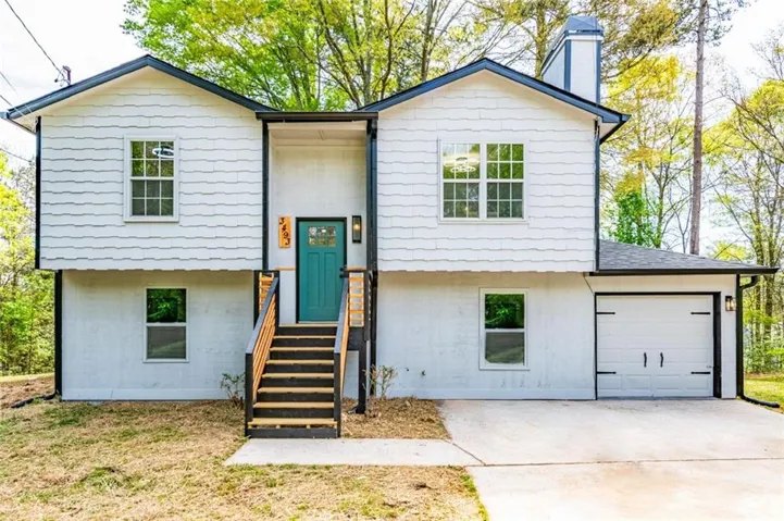 Split-level residence featuring white textured siding, a teal front door, dark trim accents, and an attached garage with a carriage-style door