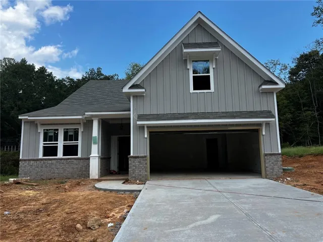 Two-story residence featuring grey vertical siding, stone veneer accents, an attached garage, a concrete driveway, and a covered entry