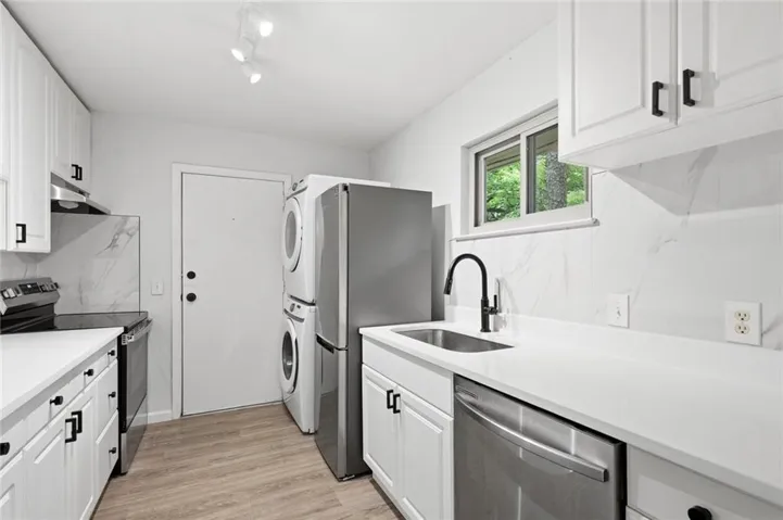 Modern kitchen featuring white cabinetry with dark hardware, solid surface countertops, and a full-height marble-look backsplash