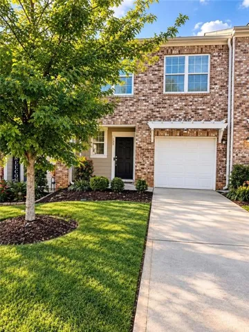 Brick exterior with white window frames, attached garage, concrete driveway, and established landscaping