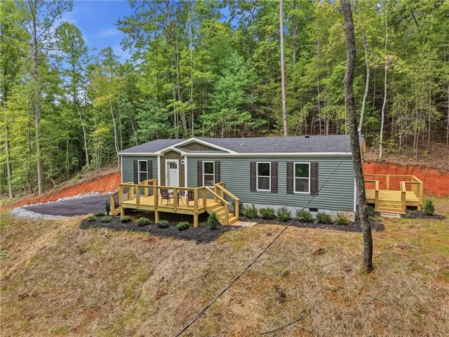 Siding exterior with shutters, wood deck, landscaped perimeter, and a gravel driveway
