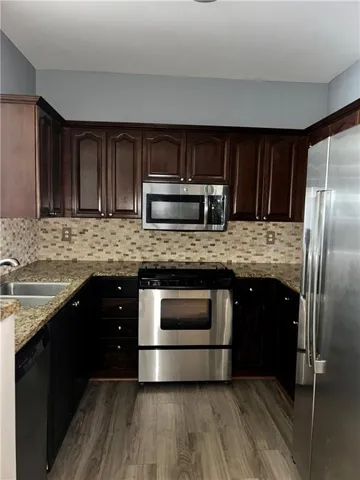 Kitchen with stainless steel appliances, dark wood finish cabinets, dark stone countertops, and dark wood-style floors