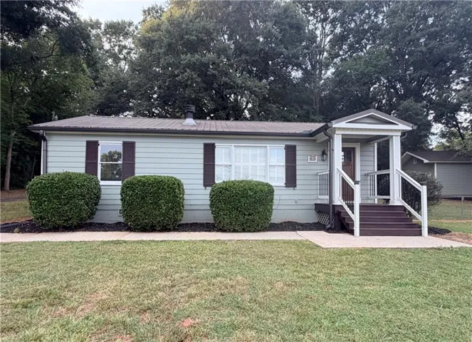 Light green siding with dark brown shutters, a covered front porch, and a metal roof