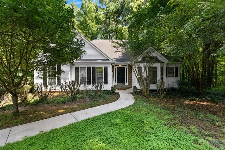 White siding exterior with dark shutters, gabled roofline, stone accents, concrete walkway, and established trees