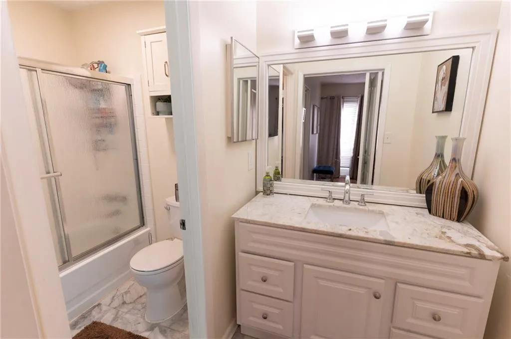 Bathroom featuring vanity, shower / bath combination with glass door, and light marble finish flooring