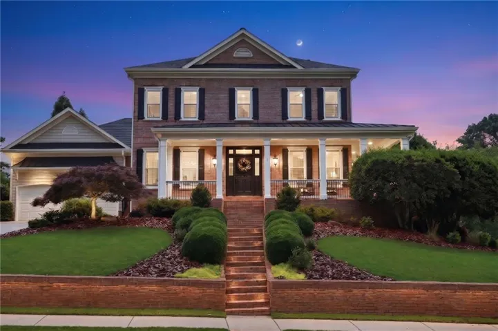 Brick exterior with white columned front porch, dark shutters, and a prominent front entry door
