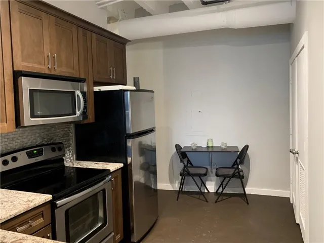 Kitchen featuring stainless steel appliances, concrete flooring, light stone countertops, and dark wood finish cabinets