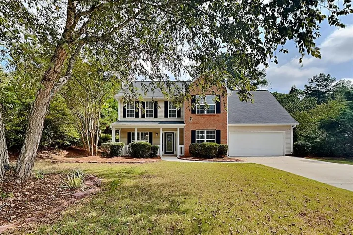 Two-story residence featuring a brick facade, covered porch, white columns, two-car garage, and established landscaping