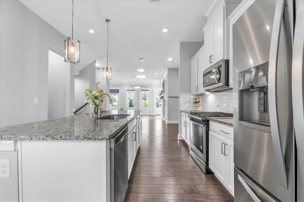 Kitchen with stainless steel appliances, white cabinetry, pendant lighting, an island with sink, and light stone countertops