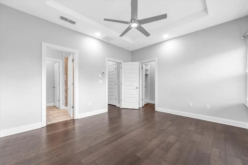 Unfurnished bedroom featuring a spacious closet, dark wood-type flooring, a tray ceiling, a ceiling fan, and recessed lighting