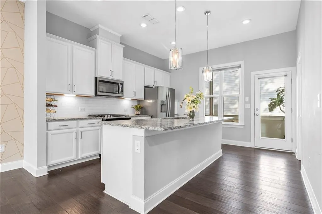 Kitchen featuring light stone countertops, white cabinets, a center island with sink, backsplash, and recessed lighting