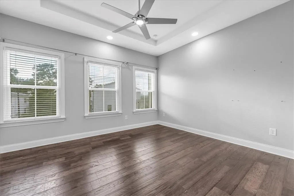 Empty room featuring a raised ceiling, dark wood-style floors, ceiling fan, and recessed lighting