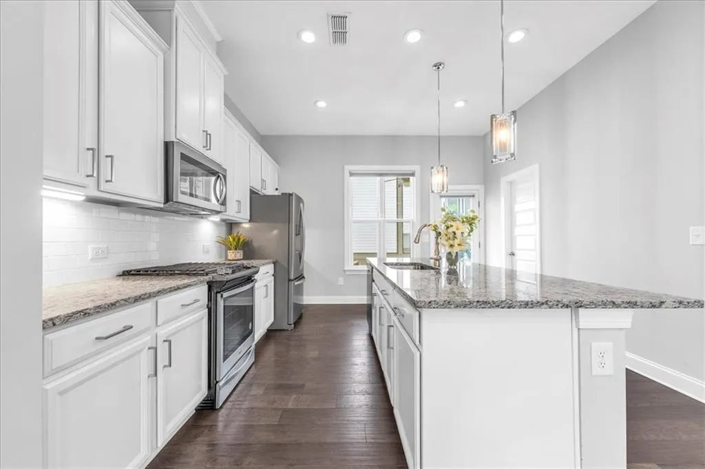 Kitchen with stainless steel appliances, light stone counters, a center island with sink, recessed lighting, and dark wood-style floors