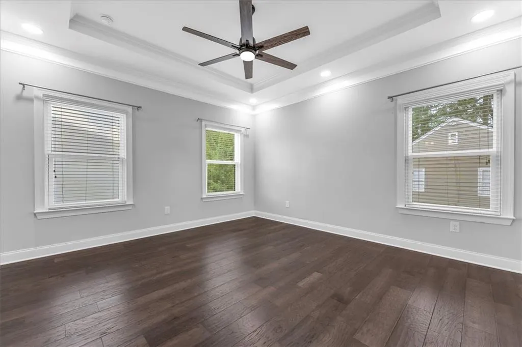 Empty room with a tray ceiling, dark wood-style floors, crown molding, recessed lighting, and ceiling fan