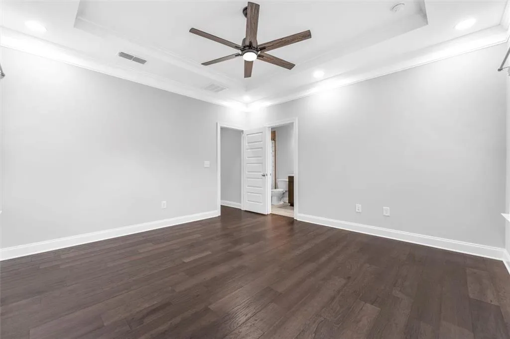 Unfurnished bedroom featuring dark wood-type flooring, a raised ceiling, ceiling fan, recessed lighting, and ornamental molding