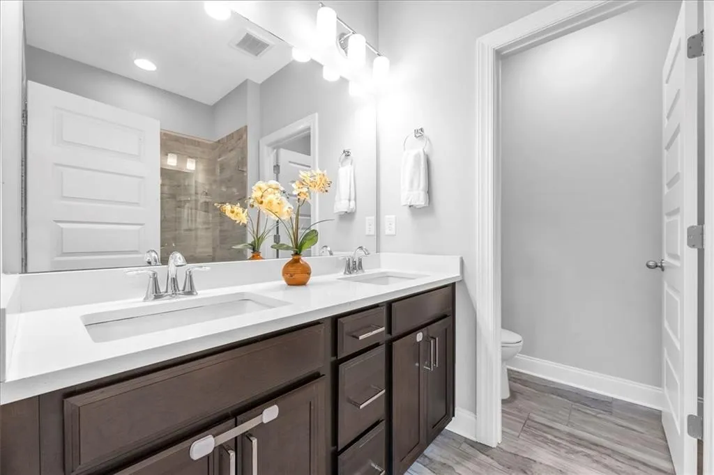 Full bathroom featuring double vanity, a shower stall, and light wood-style flooring