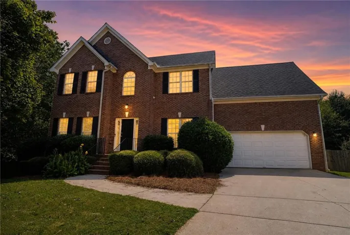 Brick exterior with dark shutters, attached two-car garage, concrete driveway, and manicured landscaping
