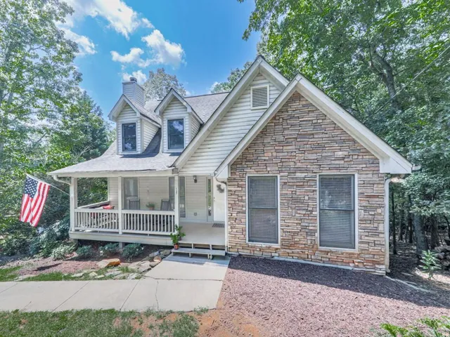 Gable-roofed home featuring stone veneer accents, white siding, and a covered front porch with white railings