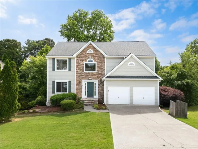 Two-story residence featuring a stone and siding facade, a two-car garage, a dark green entry door, and a manicured lawn