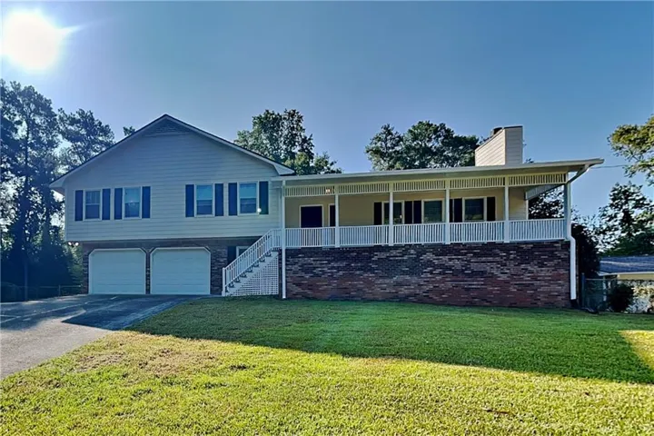 Split-level residence featuring a brick and siding exterior, a covered porch with a white railing, and a two-car garage