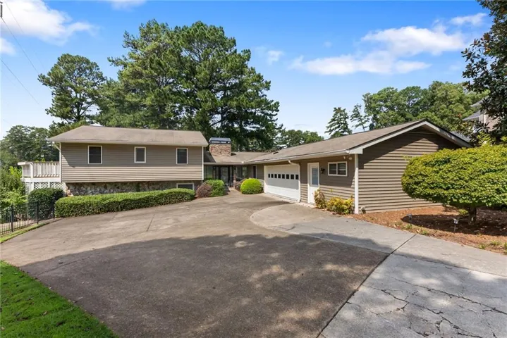 Multi-level exterior with stone and siding accents, featuring a two-car garage, expansive paved driveway, and mature landscaping