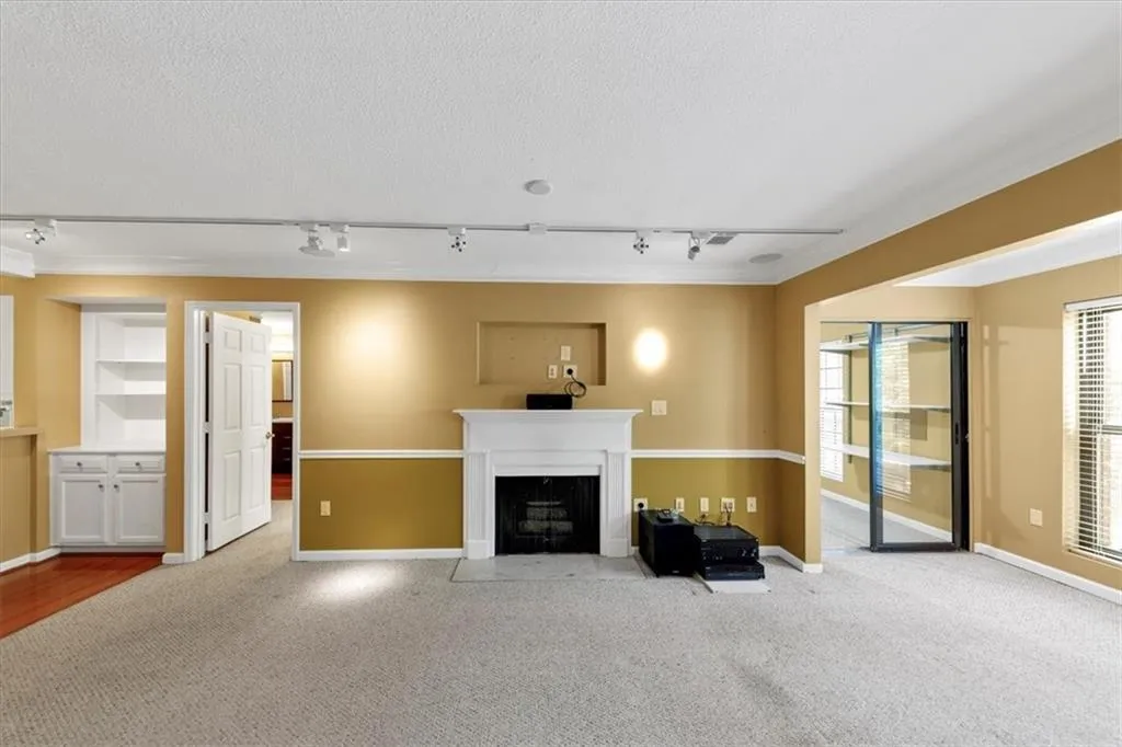 Unfurnished living room featuring track lighting, carpet floors, a fireplace with flush hearth, built in shelves, and crown molding