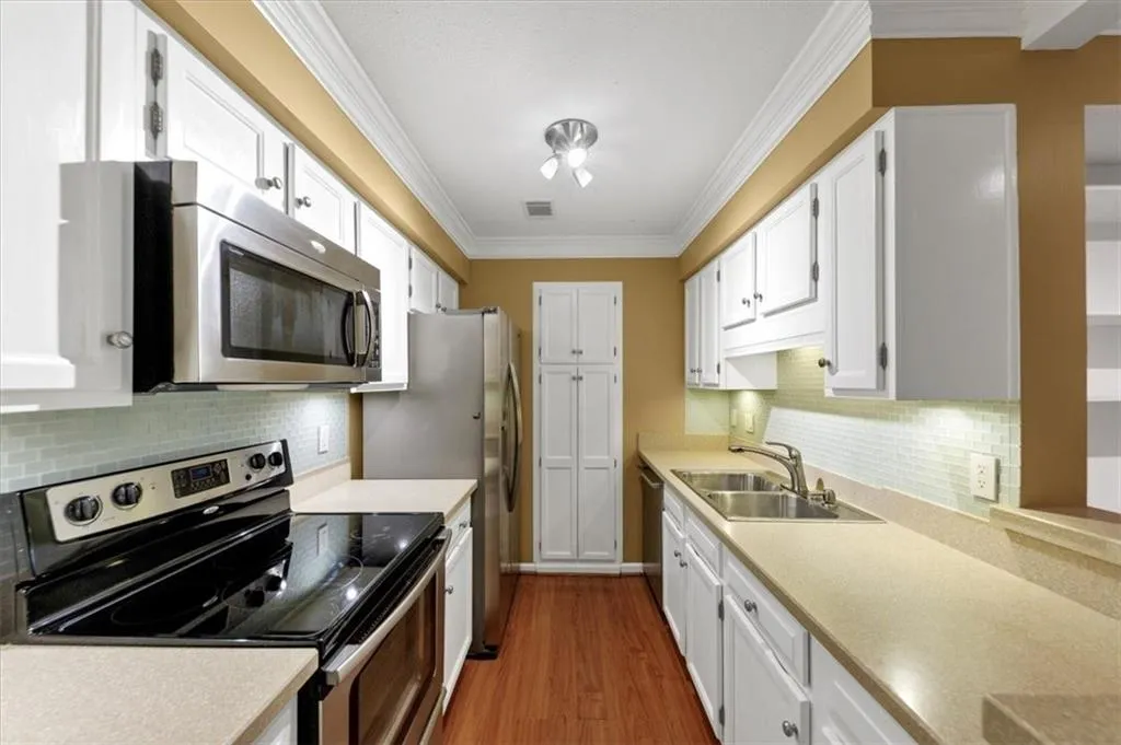 Kitchen with appliances with stainless steel finishes, backsplash, white cabinets, crown molding, and dark wood-type flooring