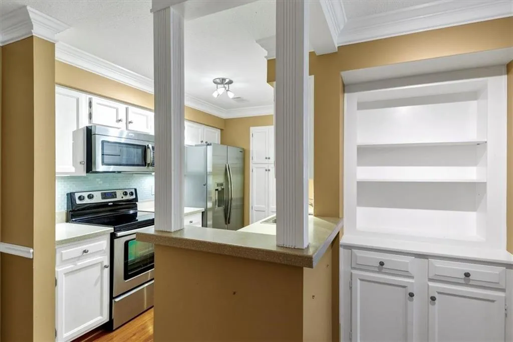 Kitchen with stainless steel appliances, white cabinets, crown molding, decorative backsplash, and light wood-style floors