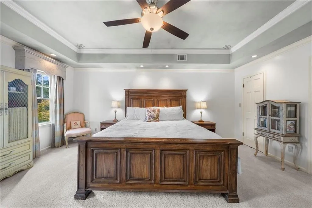 Bedroom featuring a tray ceiling, light colored carpet, ornamental molding, recessed lighting, and a ceiling fan