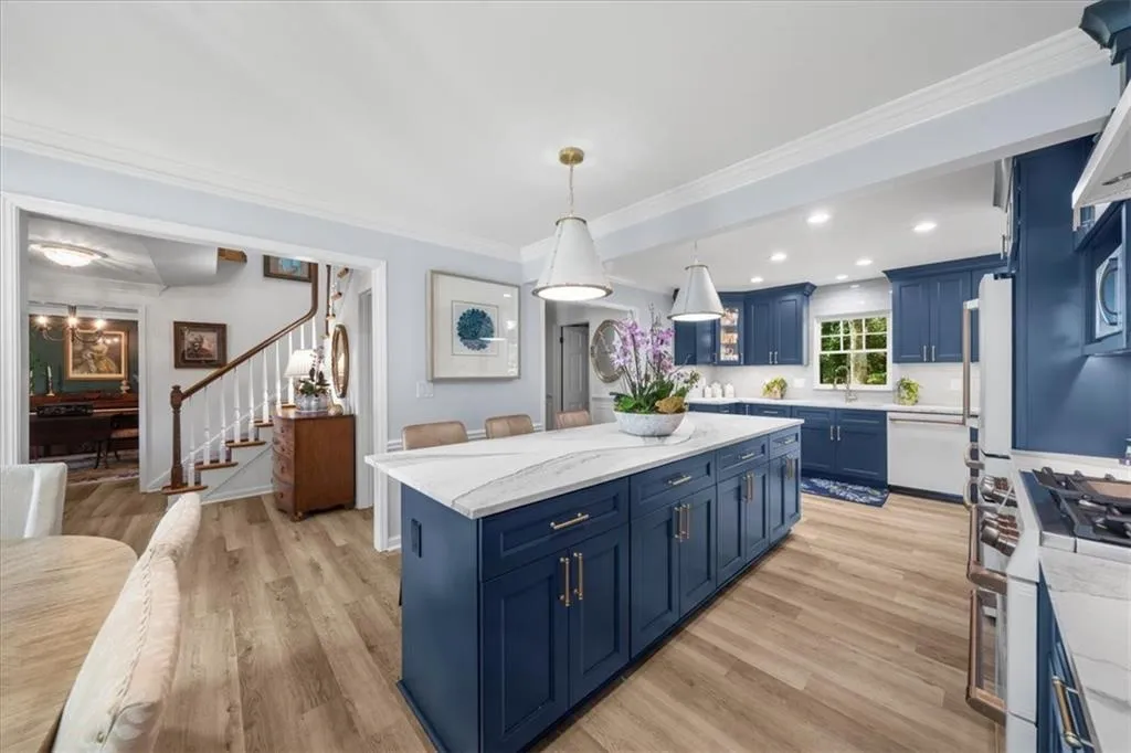 Kitchen featuring blue cabinetry, crown molding, light wood-style flooring, hanging light fixtures, and light stone countertops