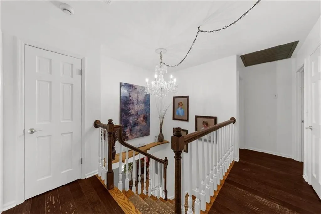Hallway featuring an upstairs landing, dark wood-type flooring, and a chandelier