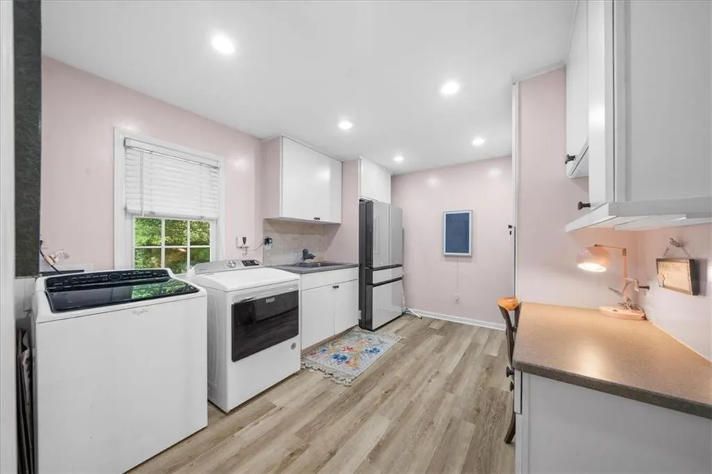 Kitchen with white cabinetry, light wood-style floors, freestanding refrigerator, washing machine and dryer, and recessed lighting