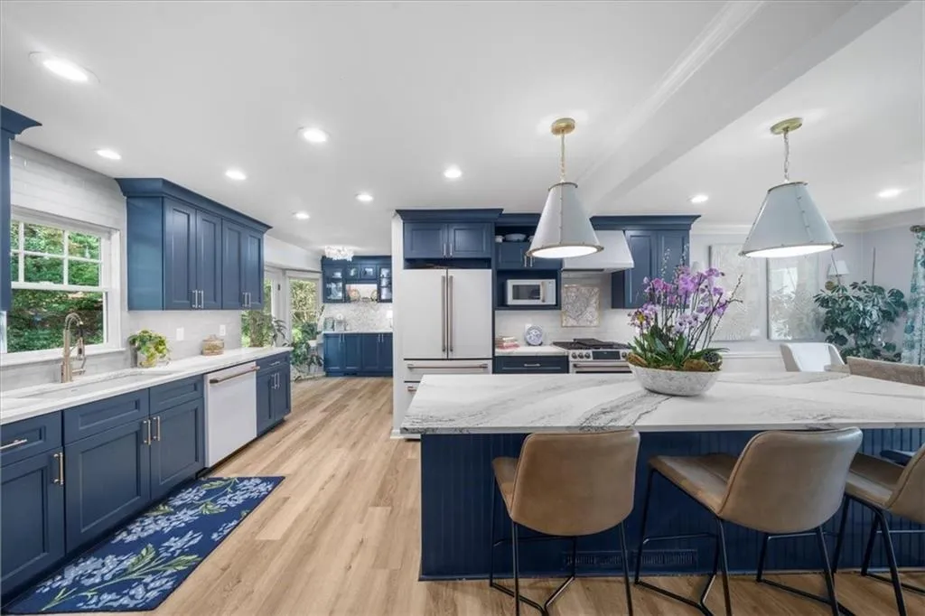Kitchen featuring blue cabinetry, light wood-style floors, light stone counters, backsplash, and a kitchen breakfast bar