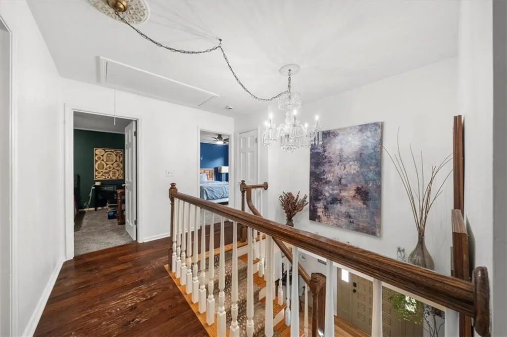 Corridor featuring an upstairs landing, dark wood-style flooring, attic access, and a chandelier