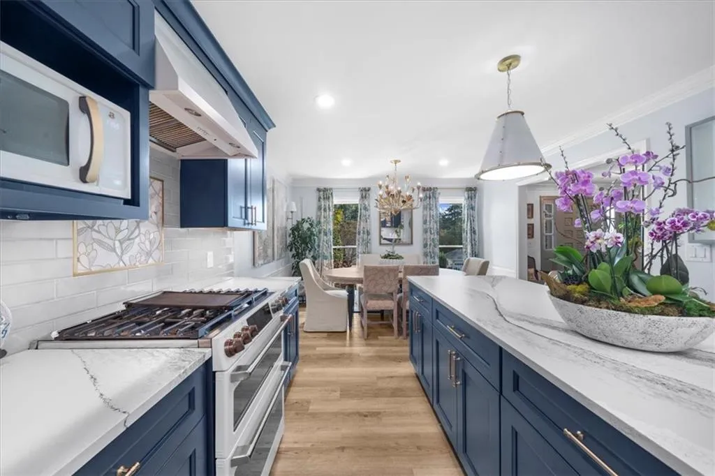 Kitchen with blue cabinets, white appliances, light stone counters, ventilation hood, and ornamental molding